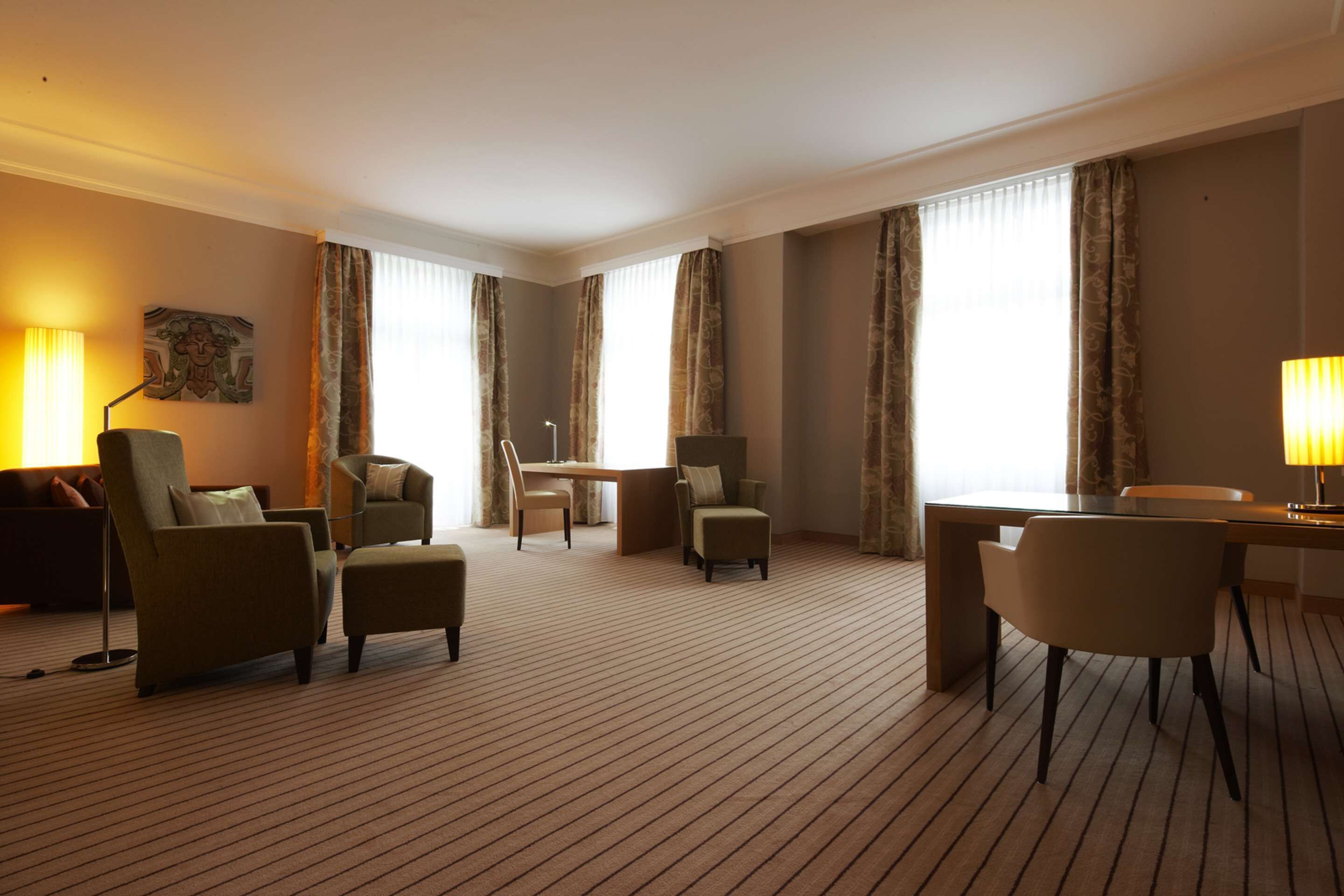 Ein Hotelzimmer mit einem großen Bett, einem Schreibtisch, zwei Sesseln, einem Sofa und einem Esstisch.