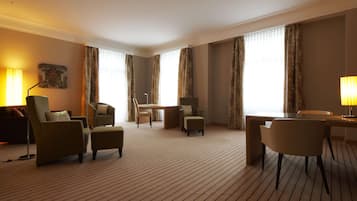 Ein Hotelzimmer mit einem großen Bett, einem Schreibtisch, zwei Sesseln, einem Sofa und einem Esstisch.