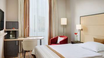 A hotel room with a bed, a desk, a chair, a TV, and a lamp.