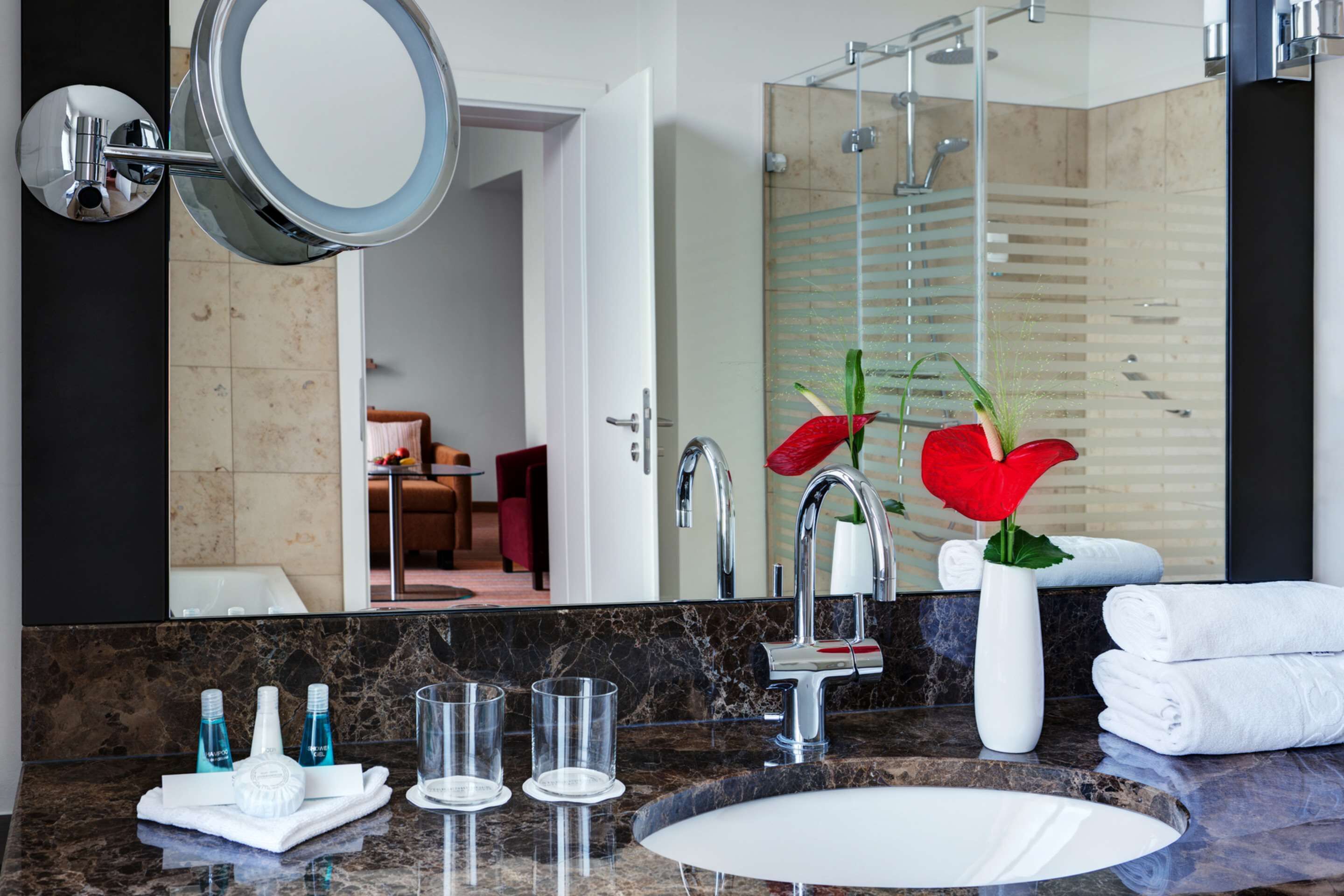 Un baño moderno con lavamanos de mármol, un espejo grande y una zona de ducha.