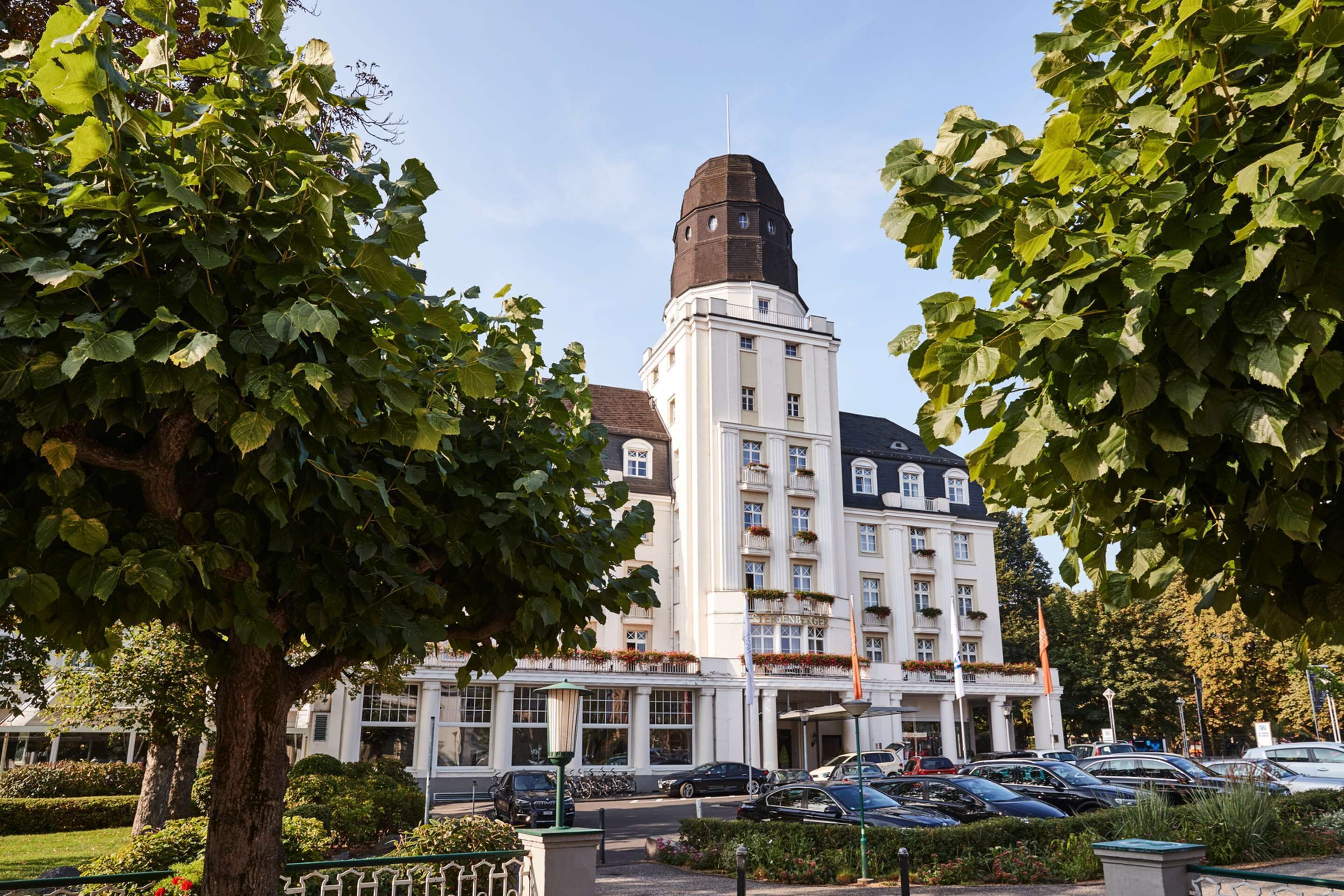 A large building with a prominent tower, surrounded by trees and parked cars.