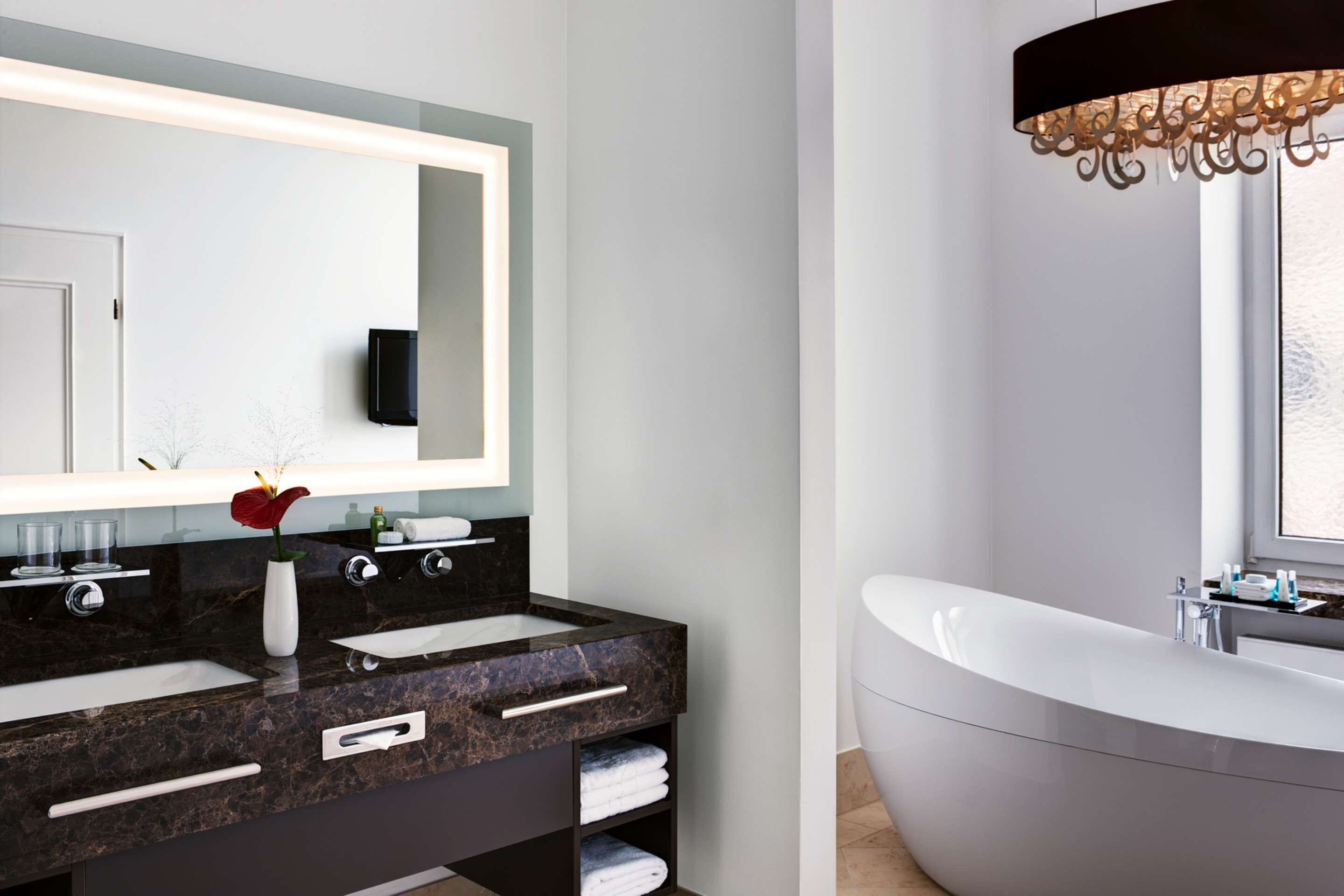 A modern bathroom with a large mirror, two sinks, a vanity, and a freestanding bathtub.