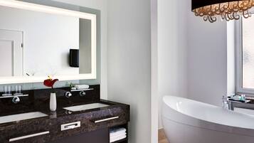 A modern bathroom with a large mirror, two sinks, a vanity, and a freestanding bathtub.