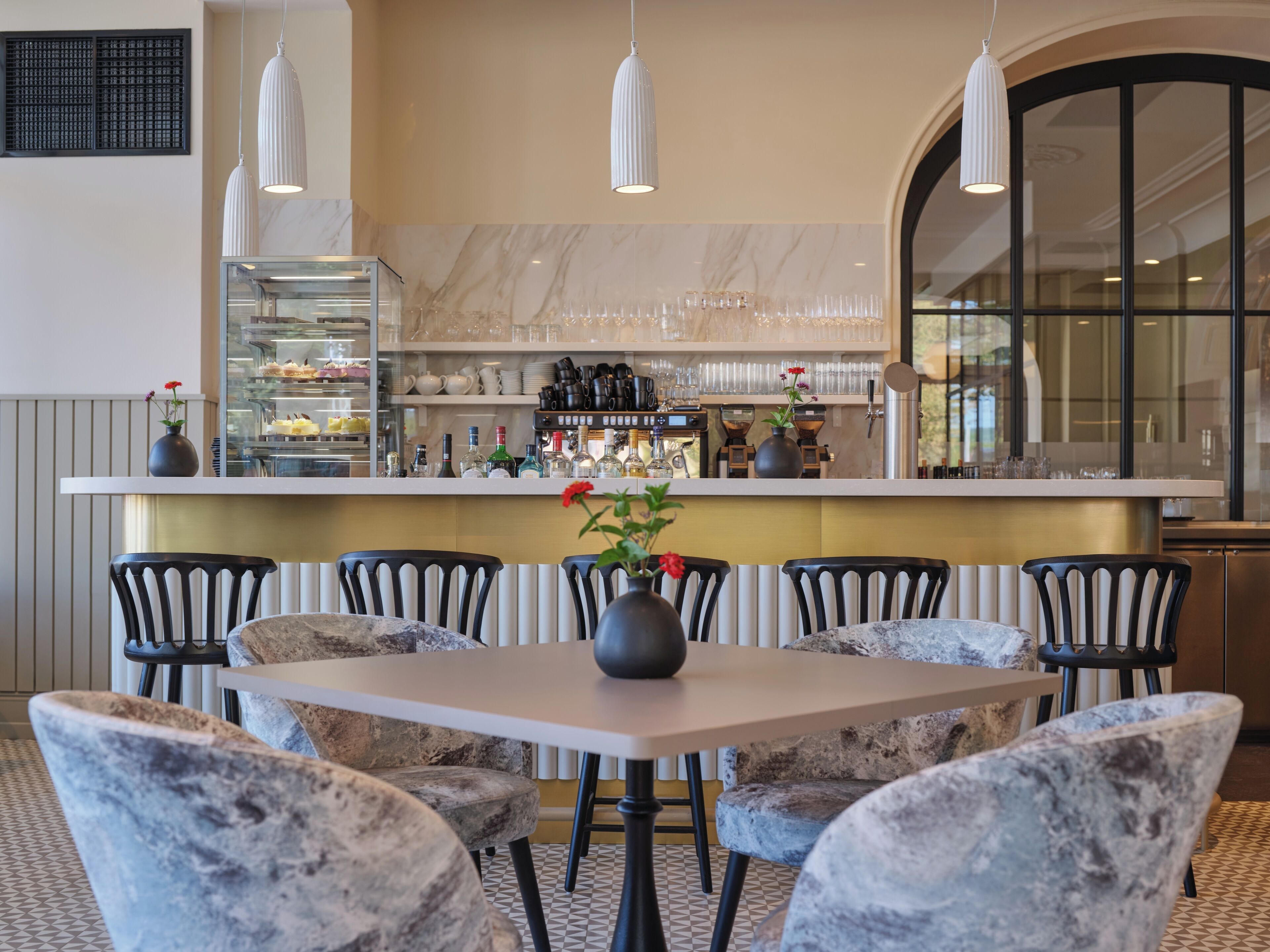 A restaurant with a marble countertop, black chairs, and a vase with flowers.
