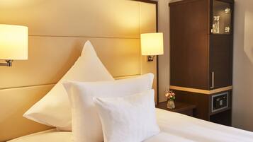 A hotel room with a bed, two bedside lamps, a nightstand with a vase of flowers, and a wooden cabinet.