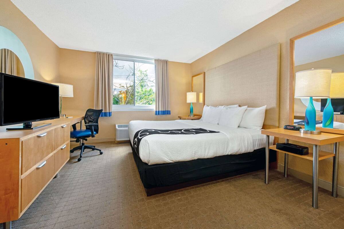 A hotel room with a bed, desk, chair, television, and a window with curtains.