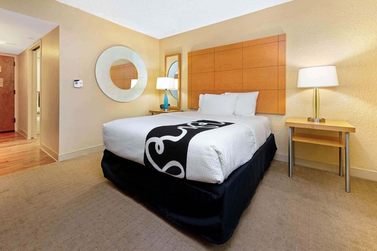 A hotel room with a large bed, a round mirror, a wooden headboard, two bedside tables with lamps, and a carpeted floor.