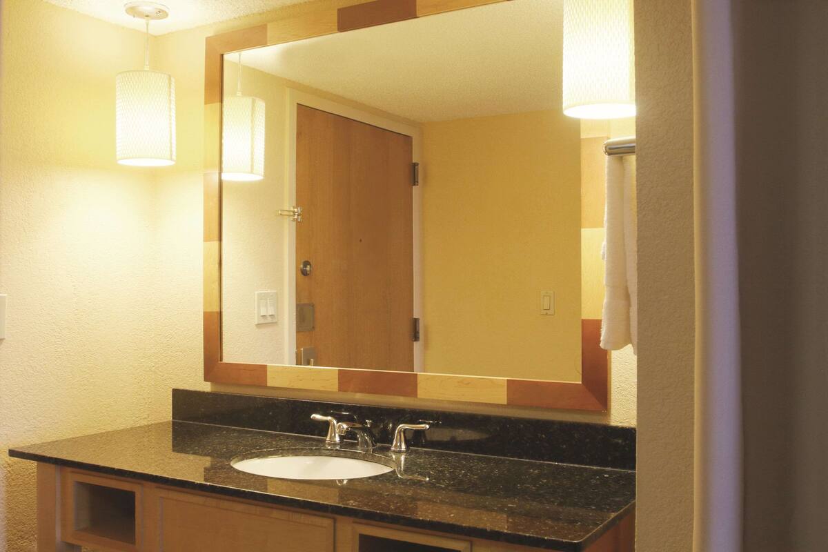 A bathroom with a large mirror, a sink, and a towel rack.