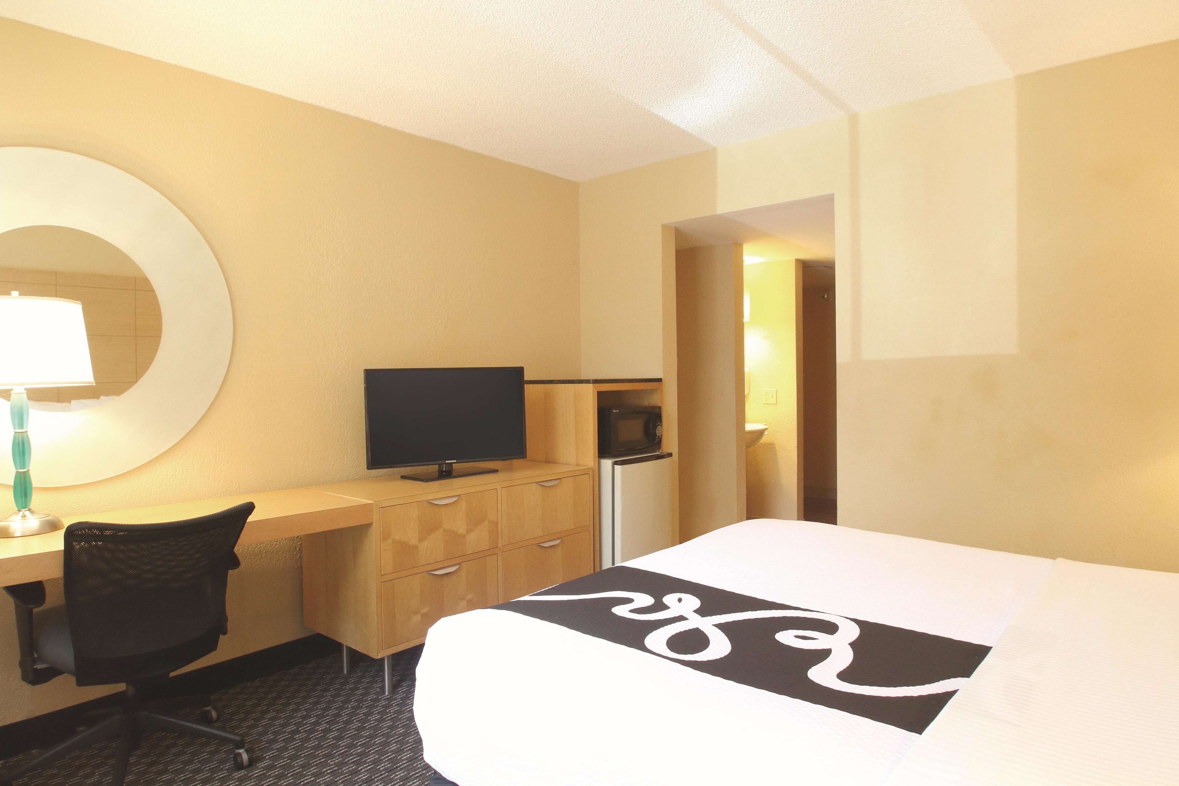 A hotel room with a bed, a desk with a computer, a chair, a TV, and a microwave.
