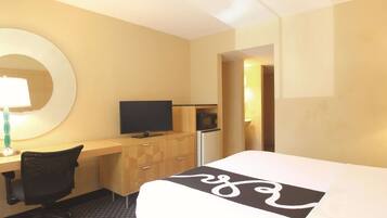 A hotel room with a bed, a desk with a computer, a chair, a TV, and a microwave.