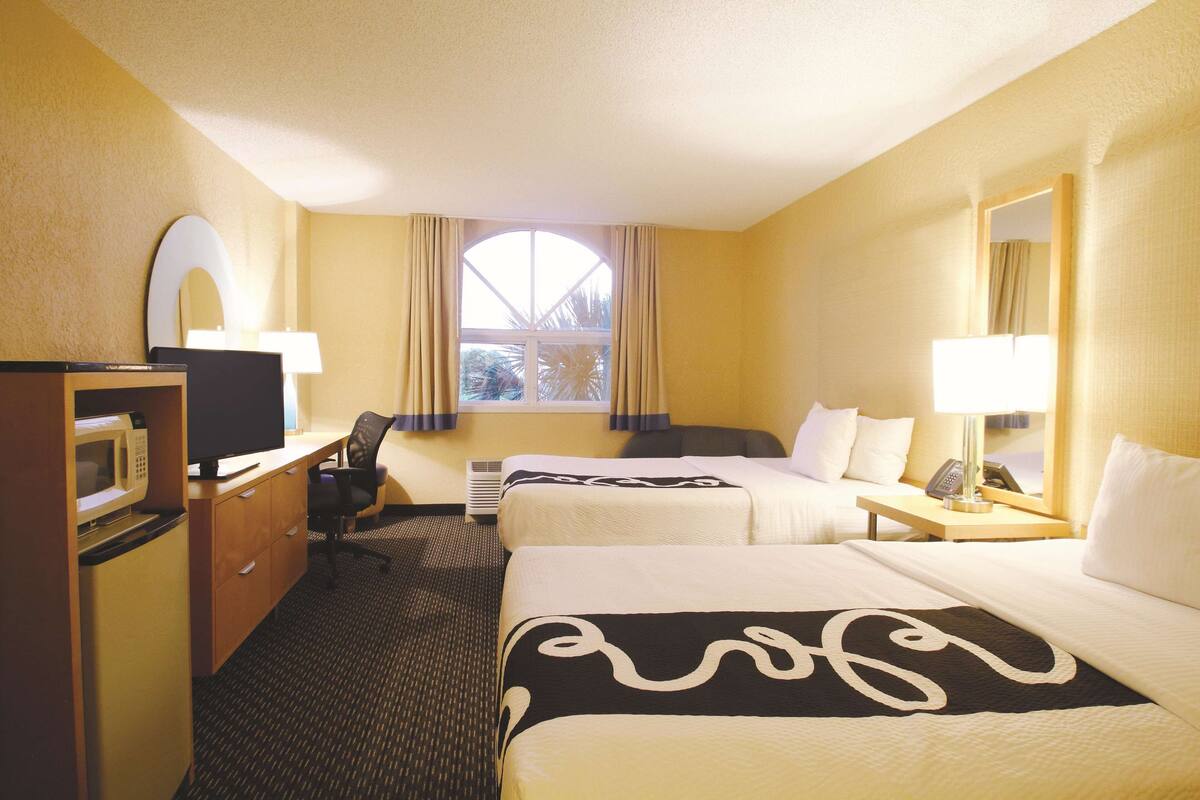 A hotel room with two beds, a desk with a computer, a TV, and a microwave.