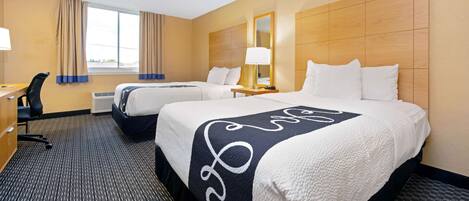 A hotel room with two beds, a desk, a chair, and a large window with curtains.