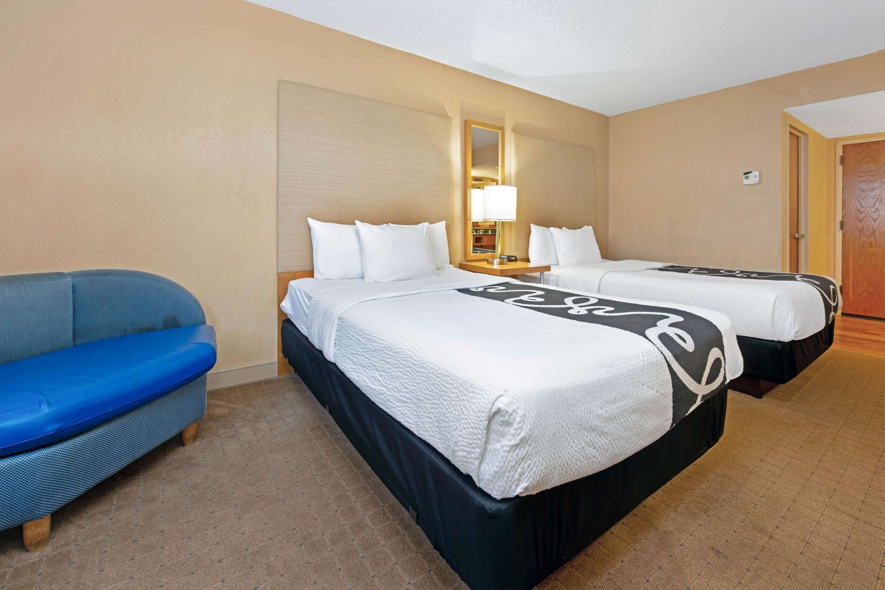 Une chambre d’hôtel avec deux lits, un canapé bleu, une table de chevet avec une lampe et un miroir au mur.