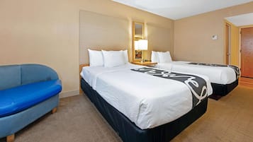Une chambre d’hôtel avec deux lits, un canapé bleu, une table de chevet avec une lampe et un miroir au mur.