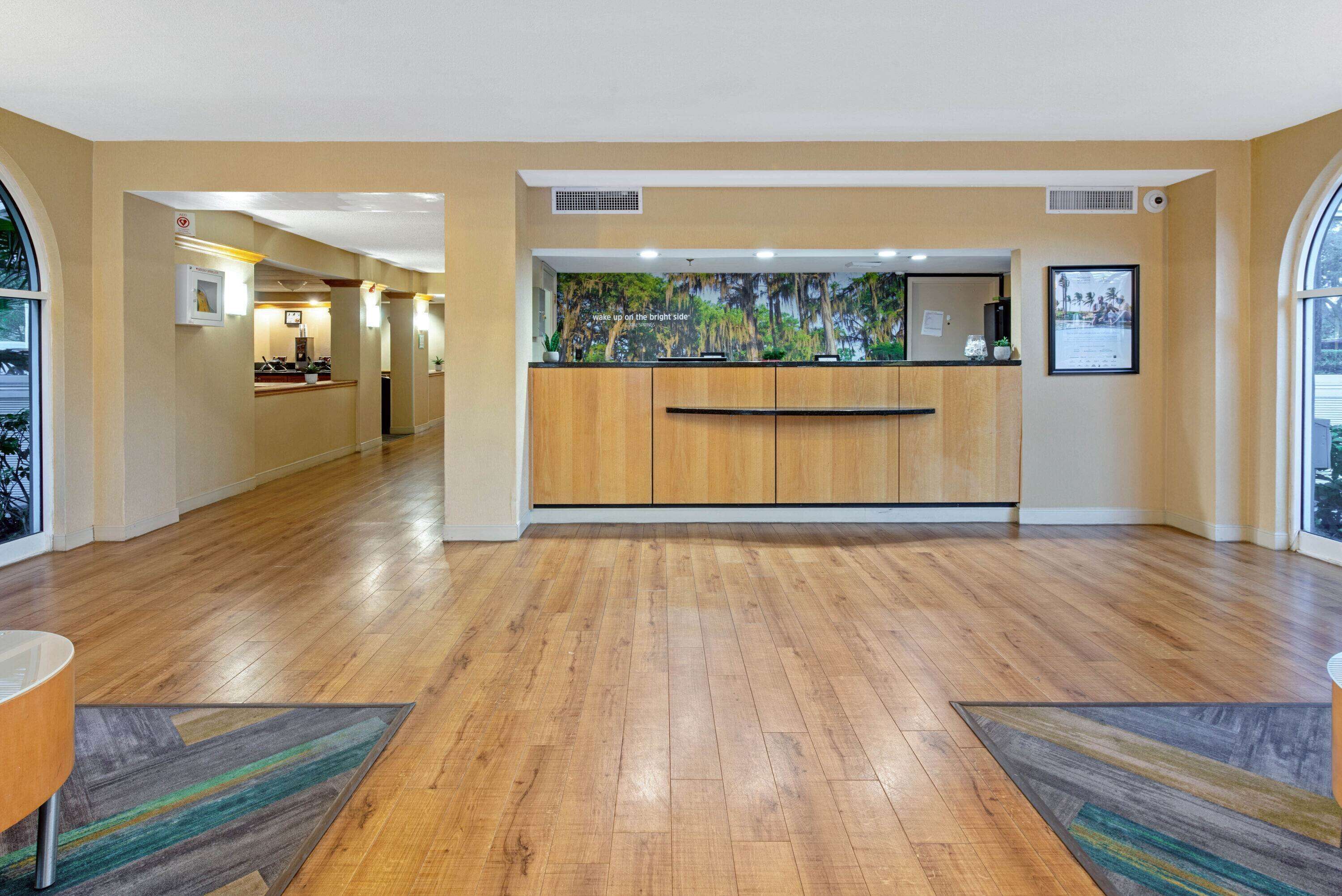 En hotellobby med trægulv, en receptionsdisk og et stort vindue.