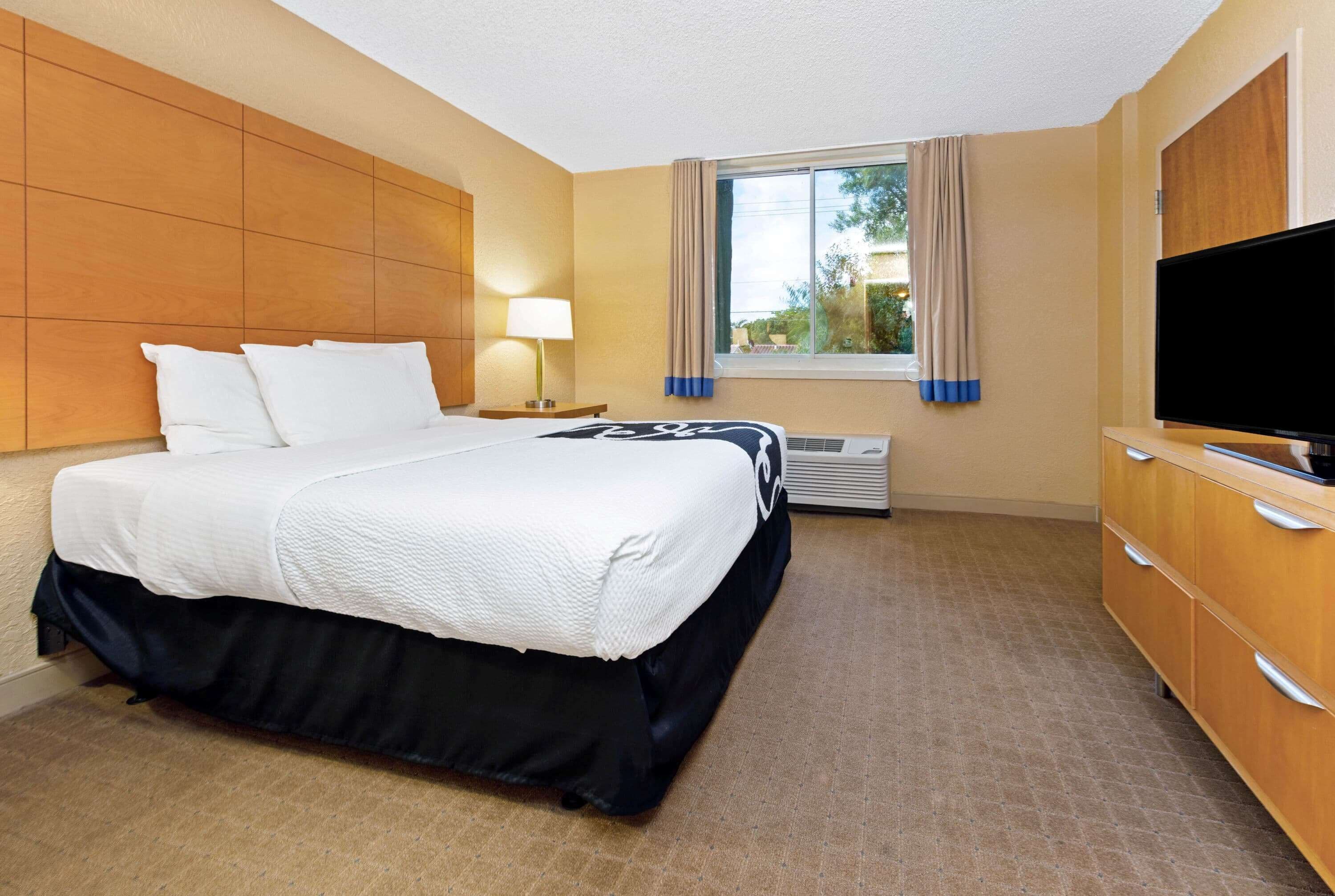 A hotel room with a bed, a TV, a desk, and a window with curtains.