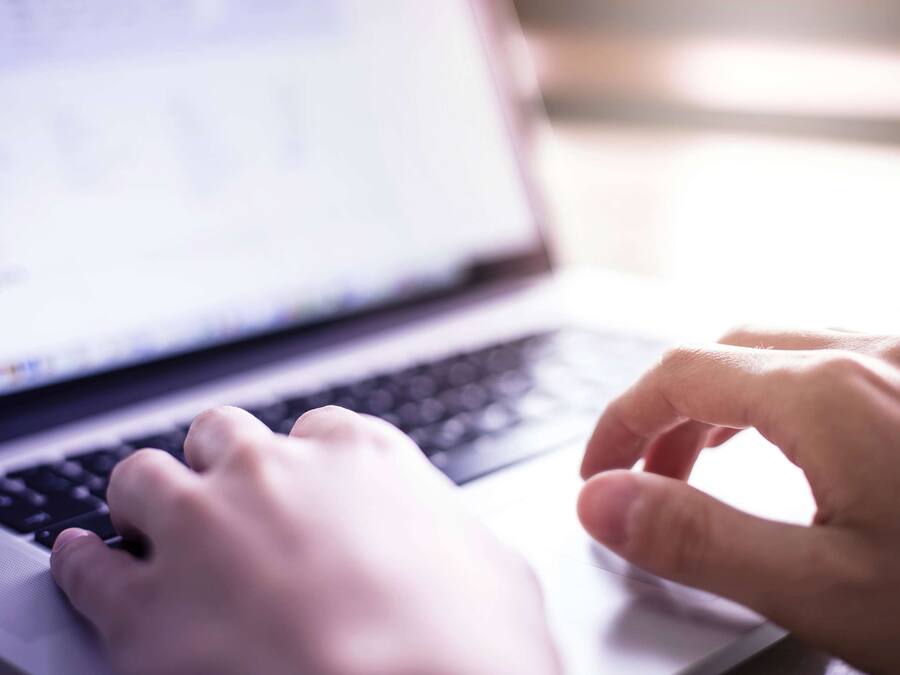A laptop with a keyboard and a person's hands typing.