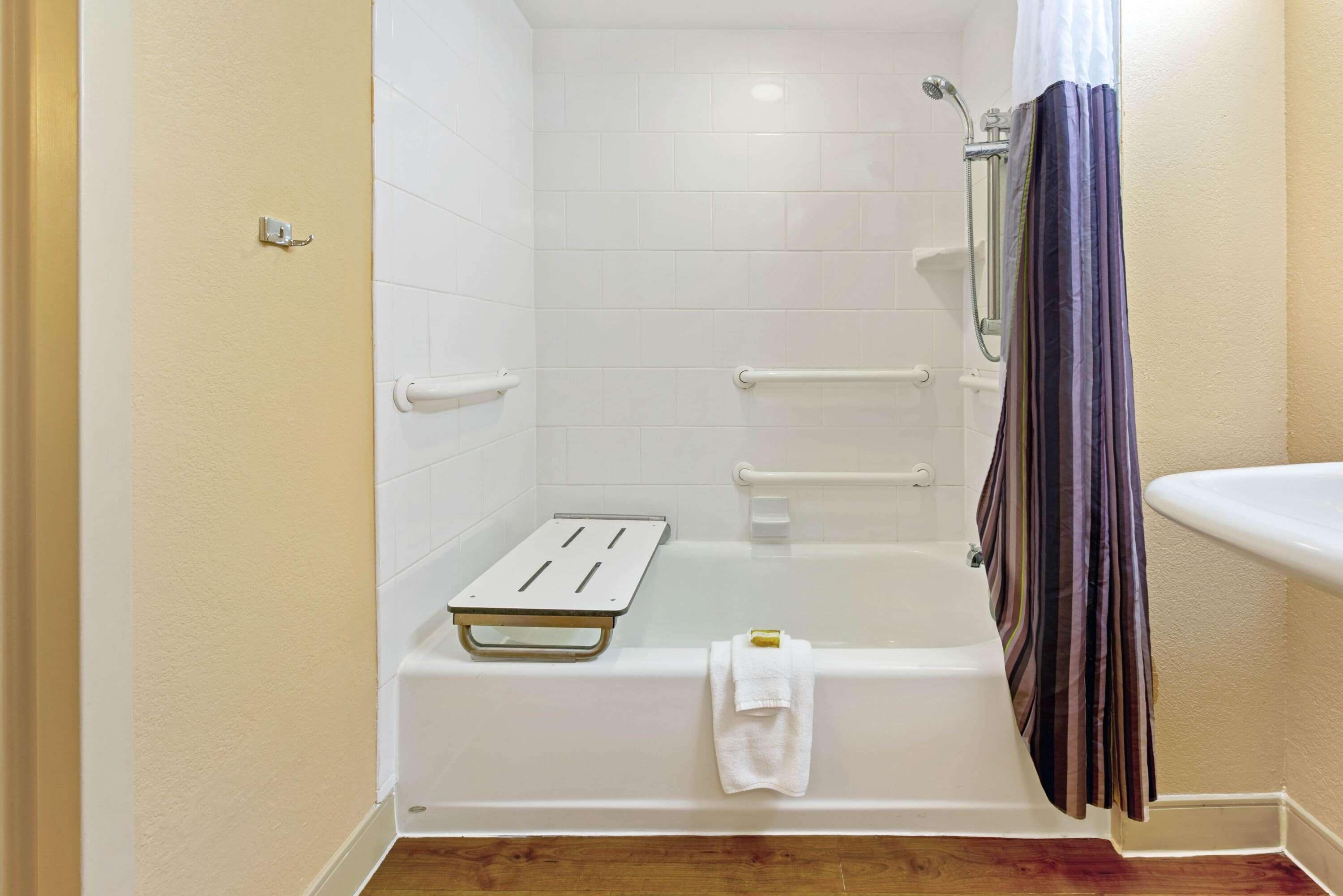 A modern bathroom with a white bathtub, a shower area, and a handrail.