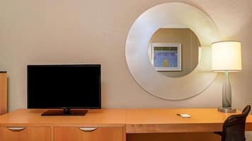 Une chambre d’hôtel avec un bureau en bois, un téléviseur à écran plat, une lampe moderne et un tableau encadré au mur.