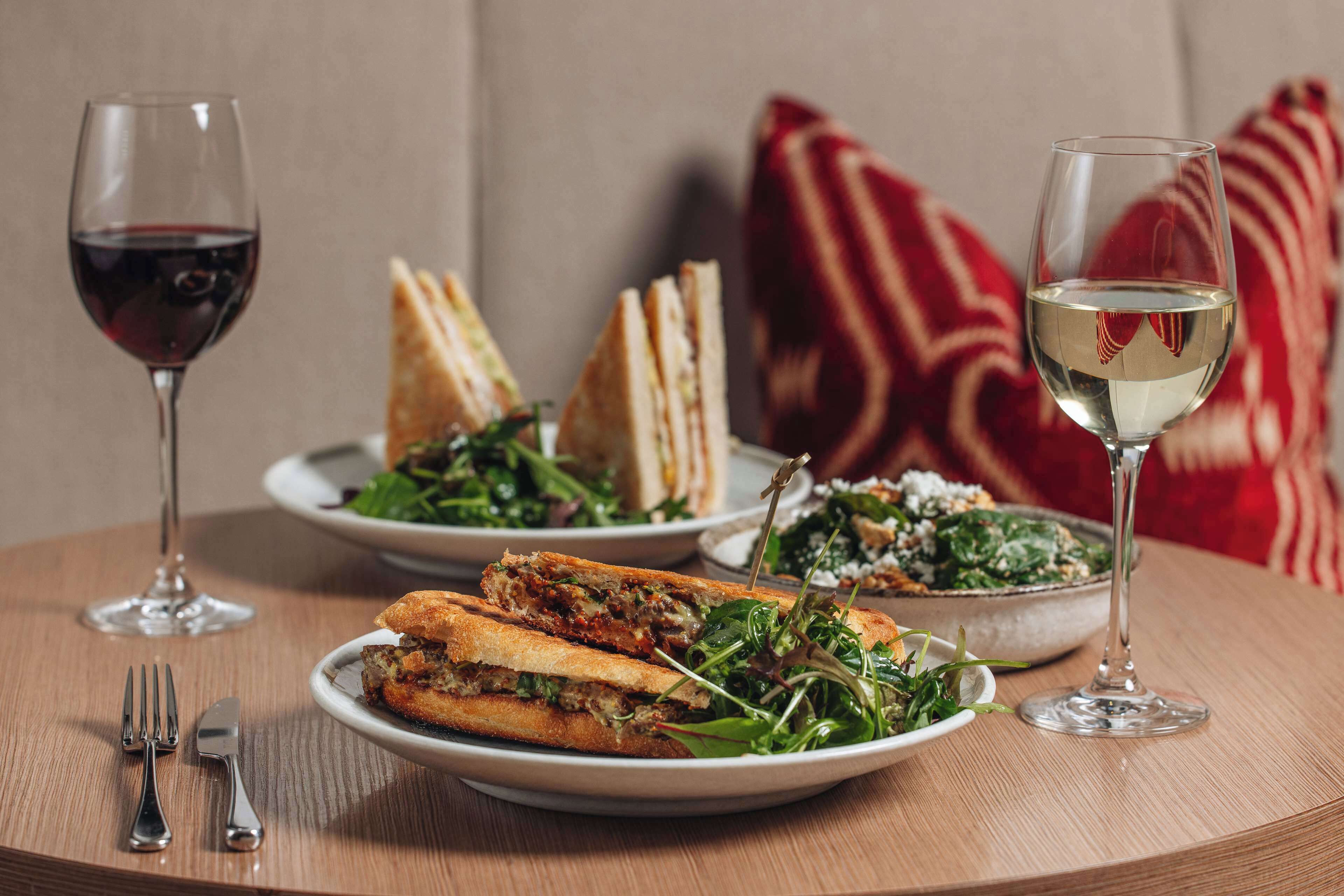 A table with a sandwich, salad, wine glasses, and cutlery.