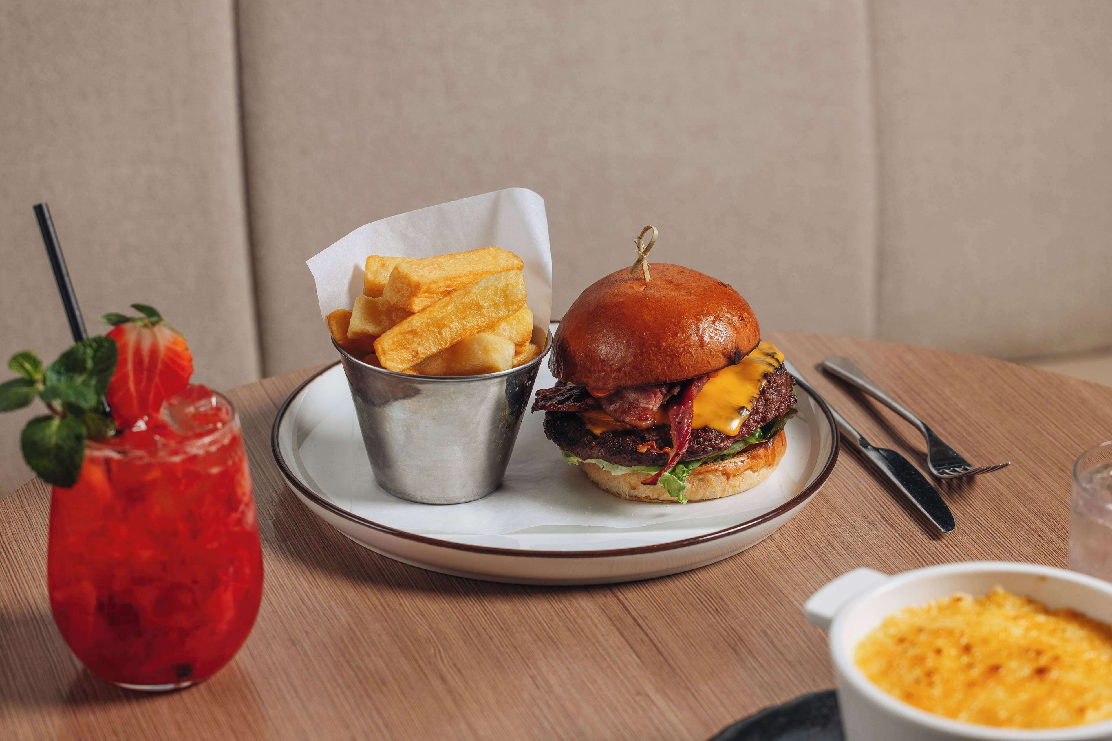 Une assiette avec un hamburger et des frites, une boisson avec une paille et un bol de macaronis au fromage.