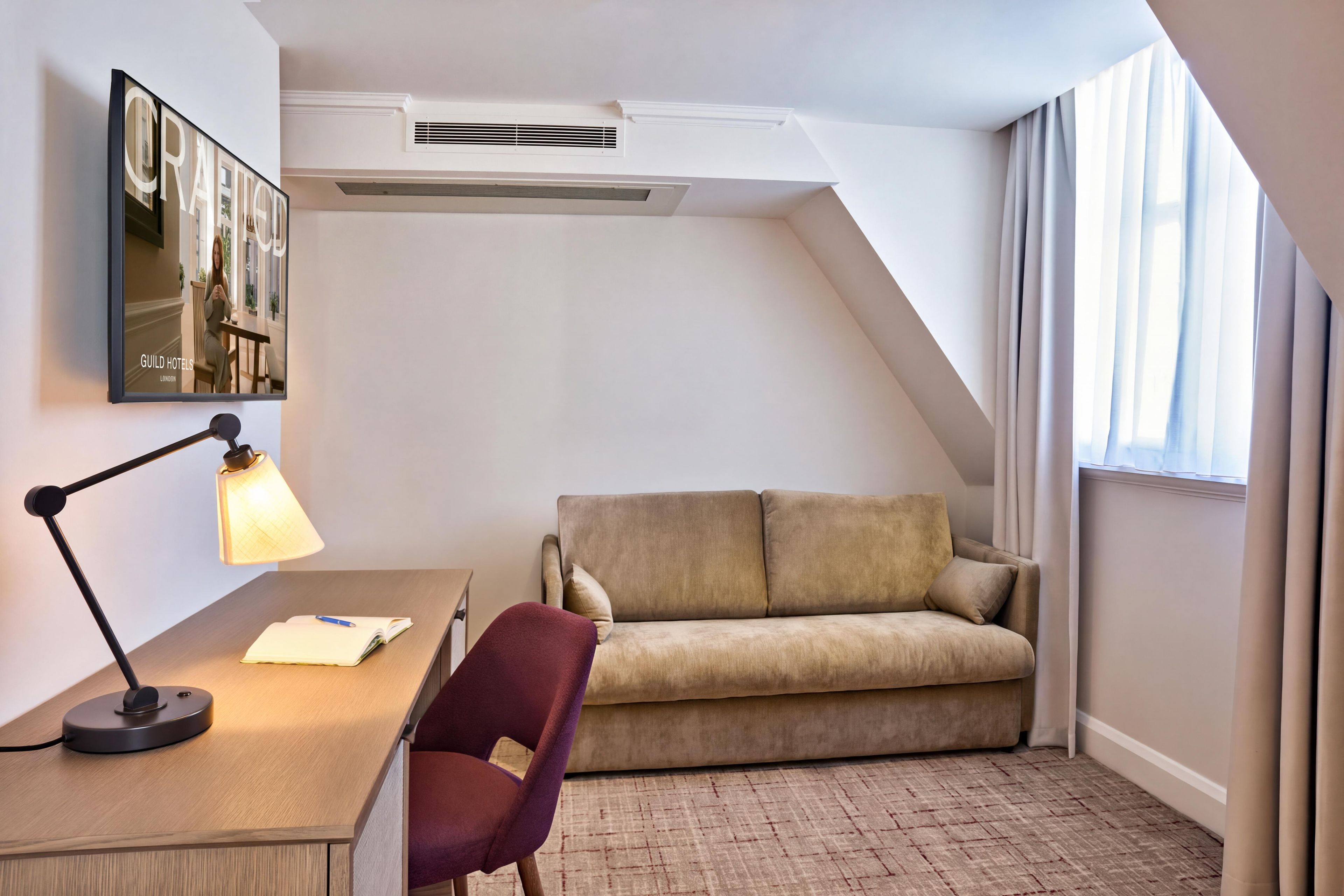 Een hotelkamer met een bureau, stoel, bank en een groot raam.
