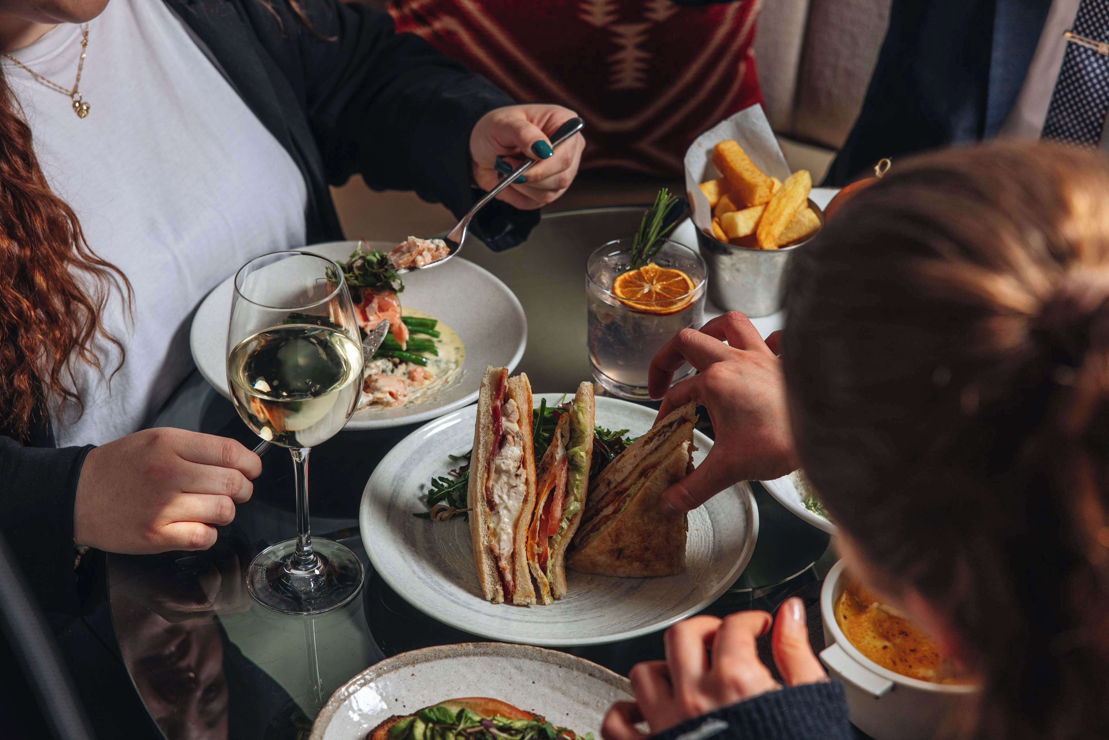A dining table with plates of food, glasses of wine, and a bowl of fries.
