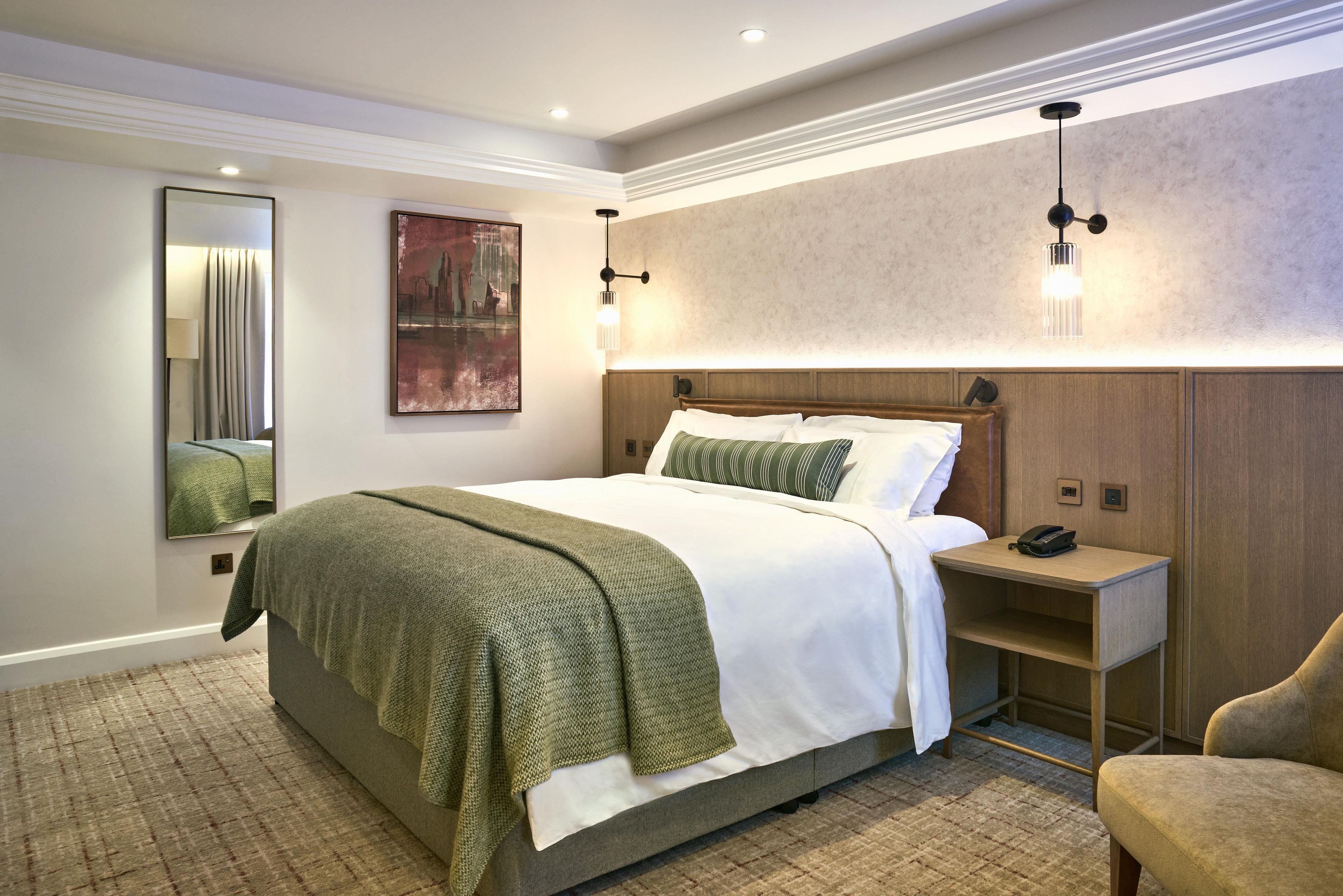 A hotel room with a large bed, bedside table, and a mirror.