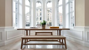Una habitación con un ventanal grande, un banco de madera, una mesita y una planta en maceta.