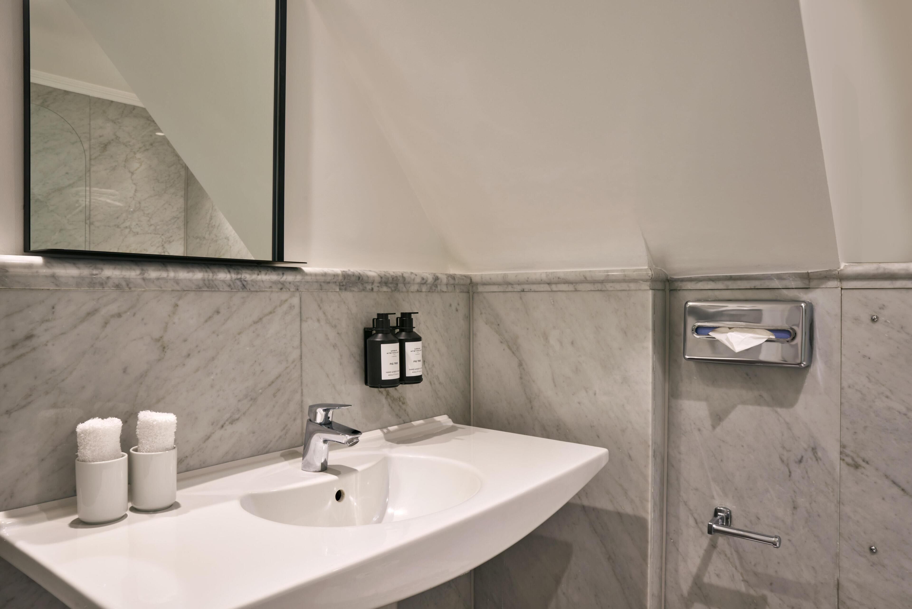 A modern bathroom with a curved white sink, a mirror, and two hand soap dispensers.