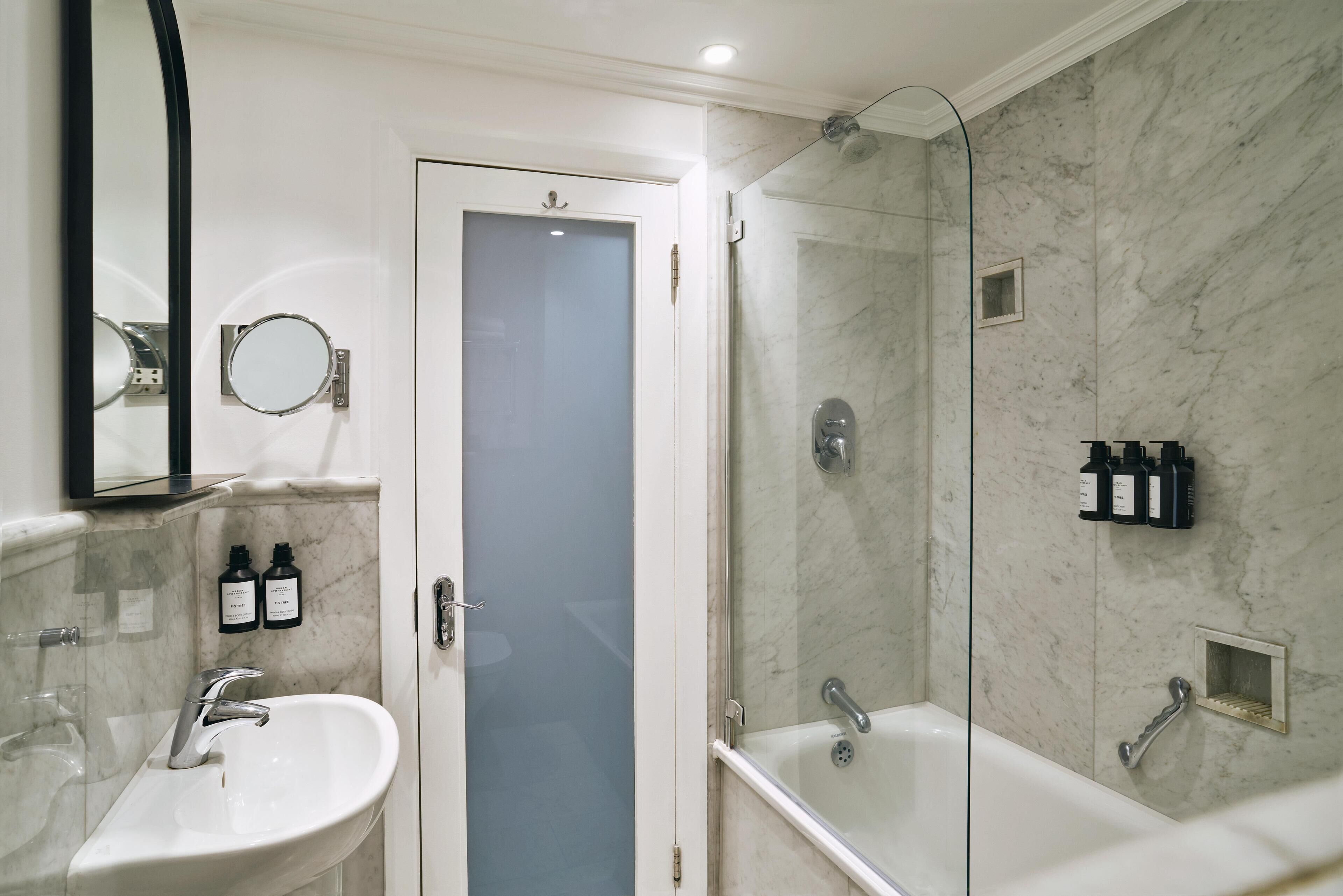 A modern bathroom with a white sink, a mirror, a shower, and a door with a frosted glass panel.