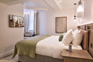 A hotel room with a bed, bedside table, lamp, artwork, and a view of the outside. - Guild Hotel Bloomsbury (London)