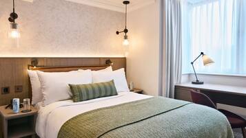 A hotel room with a bed, bedside table, lamp, and a window with curtains.