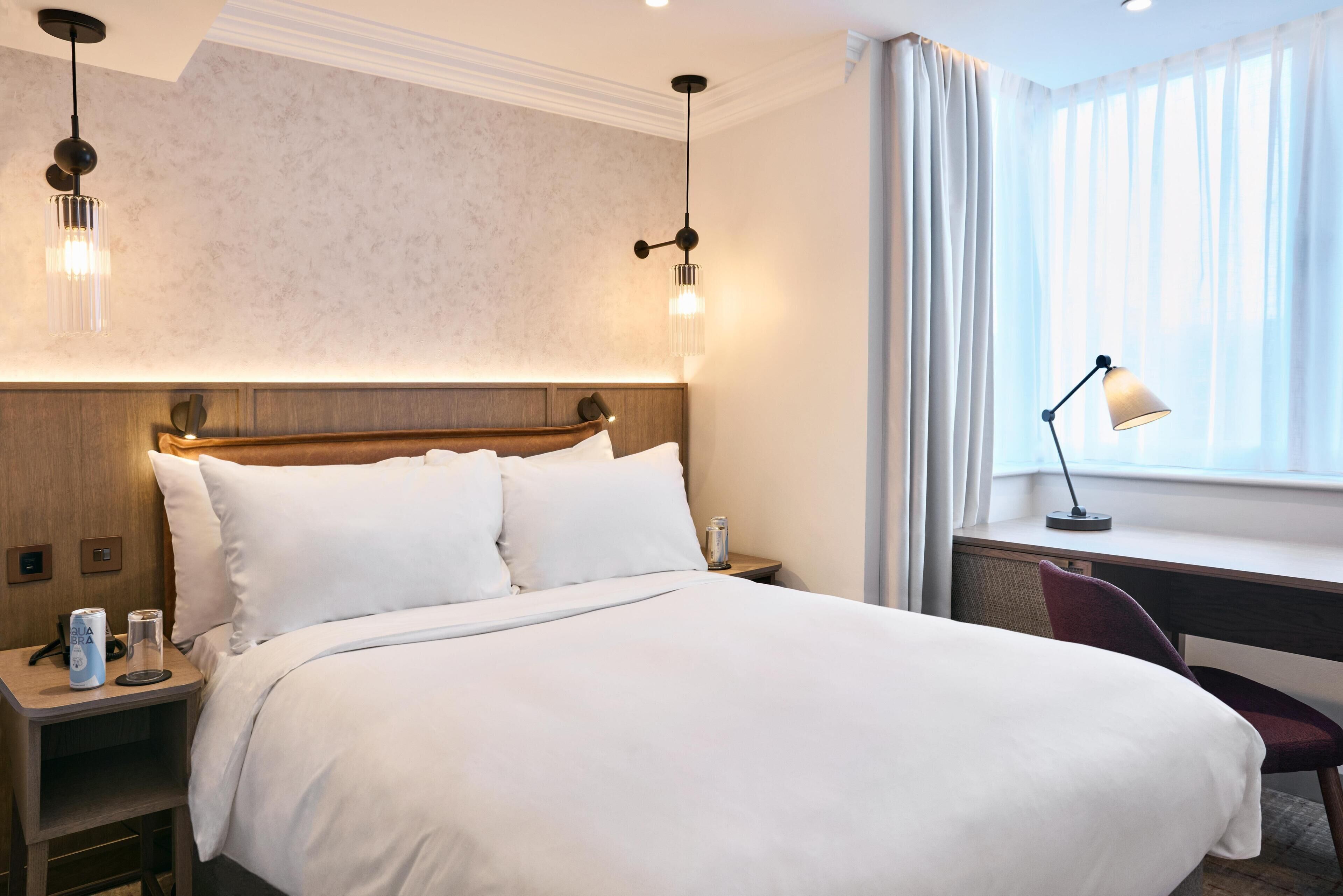 Ett hotellrum med en stor säng, sängbord, ett skrivbord och ett fönster med gardiner.