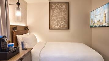 Et hotelværelse med en seng, et skrivebord med lampe, et indrammet abstrakt kunstværk og et bybillede.