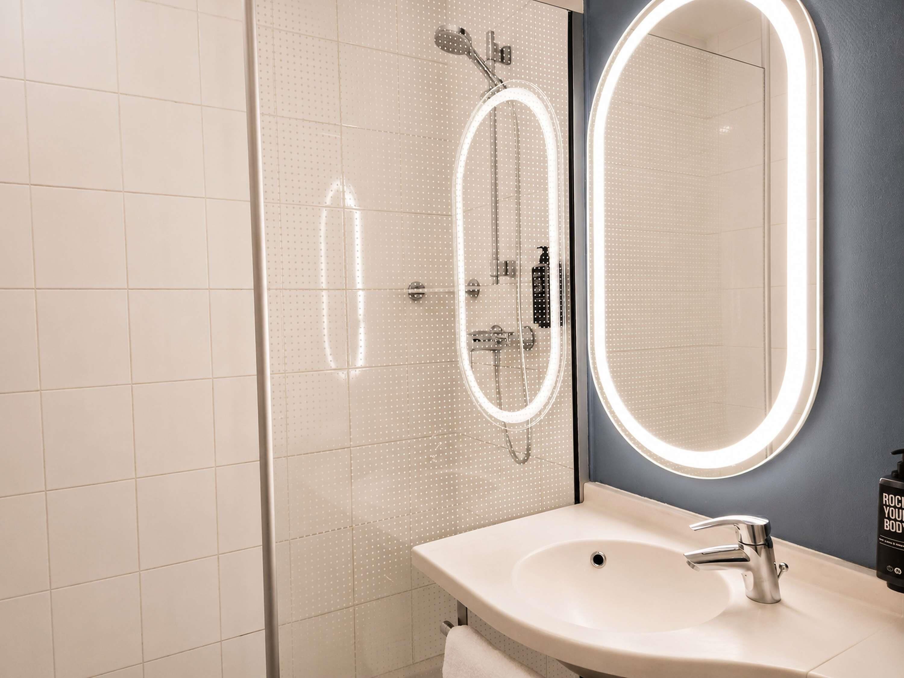 Un baño moderno con ducha acristalada, un espejo grande y un lavamanos con grifo.