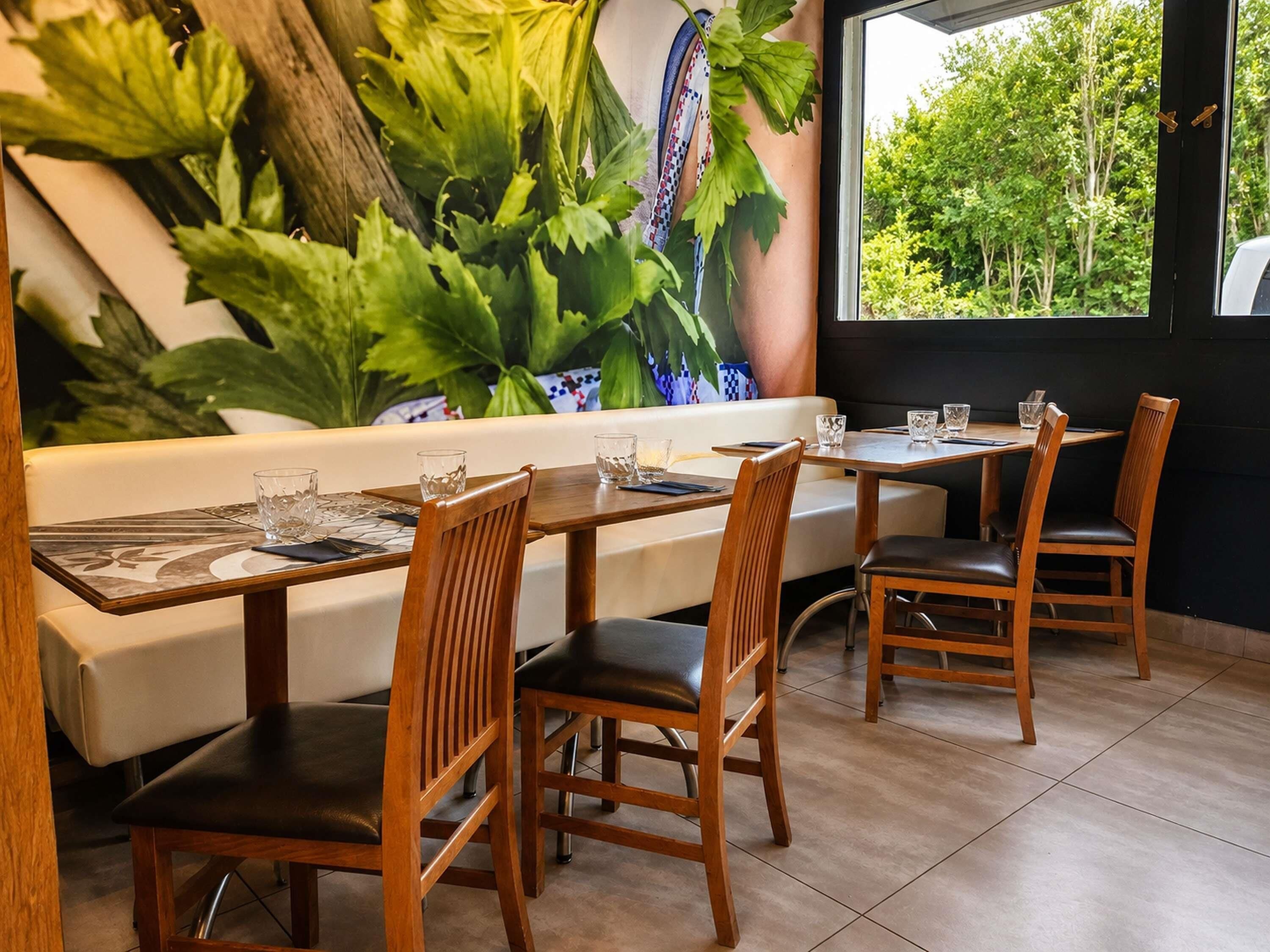 A restaurant with wooden chairs and tables, a white cushioned bench, and a large green plant wall.