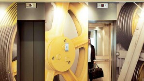An elevator with a yellow gear design, a digital display, and emergency exit signs. - ibis Paris Porte d'Italie (Gentilly)
