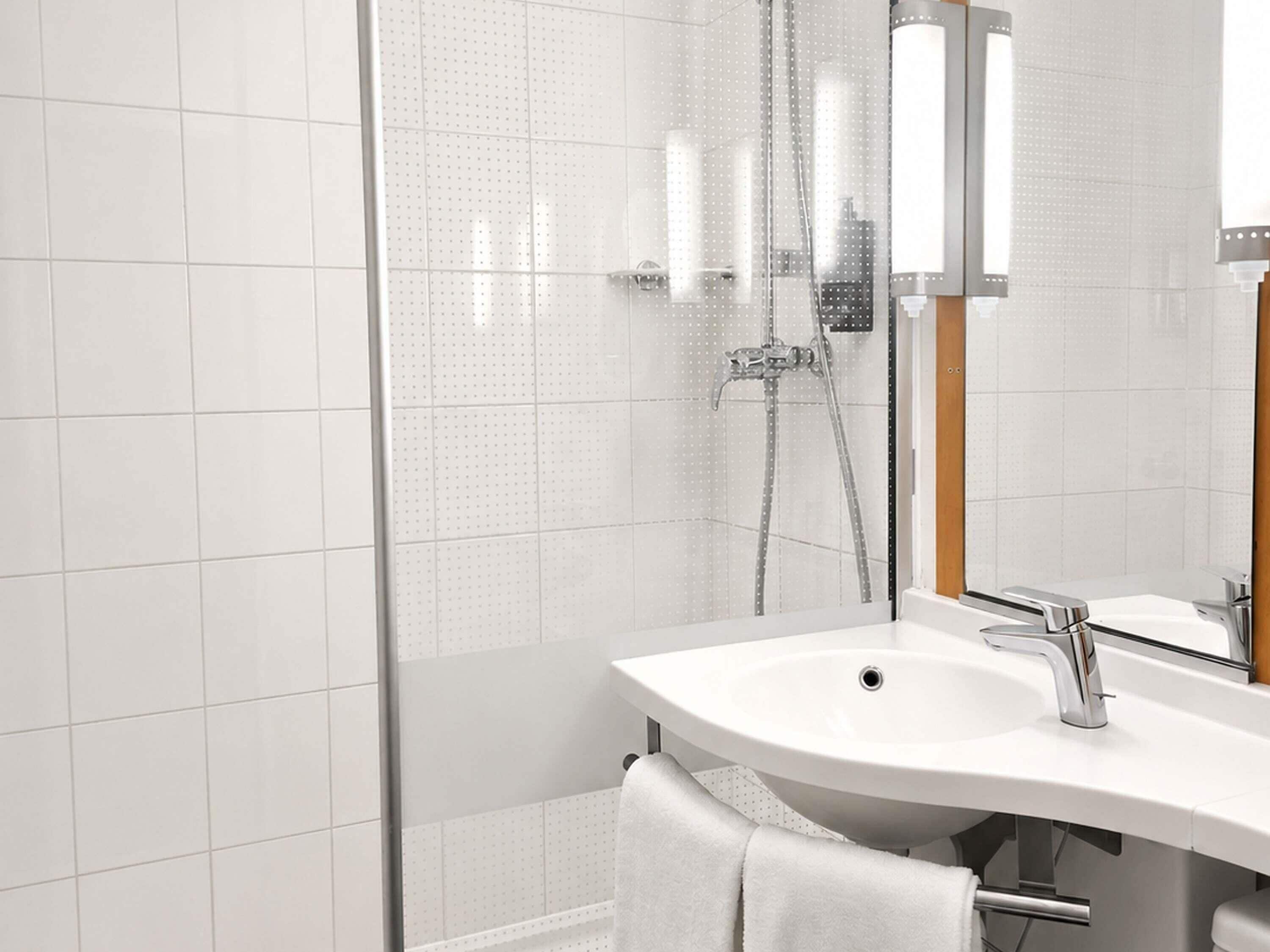 A modern bathroom with a glass shower enclosure, a white sink, and a mirror.