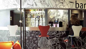 A bar area with a counter, bar stools, and a person behind the bar. - ibis Paris Porte d'Italie (Gentilly)