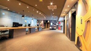 A modern reception area with a long counter, computers, and a seating area. - ibis Paris Porte d'Italie (Gentilly)