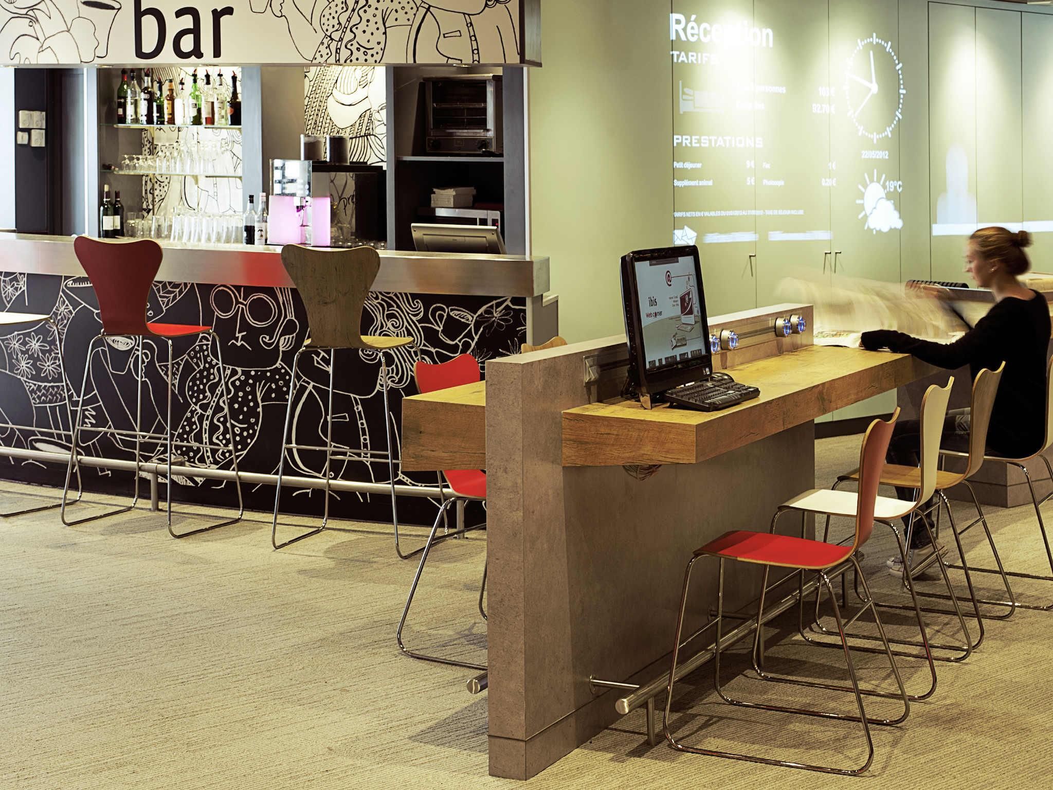 Un espace bar comprenant un comptoir, des tabourets et un écran numérique affichant des informations.
