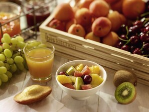 A breakfast setting with a bowl of fruit, a glass of orange juice, and a crate of peaches. - ibis Paris Porte d'Italie (Gentilly)