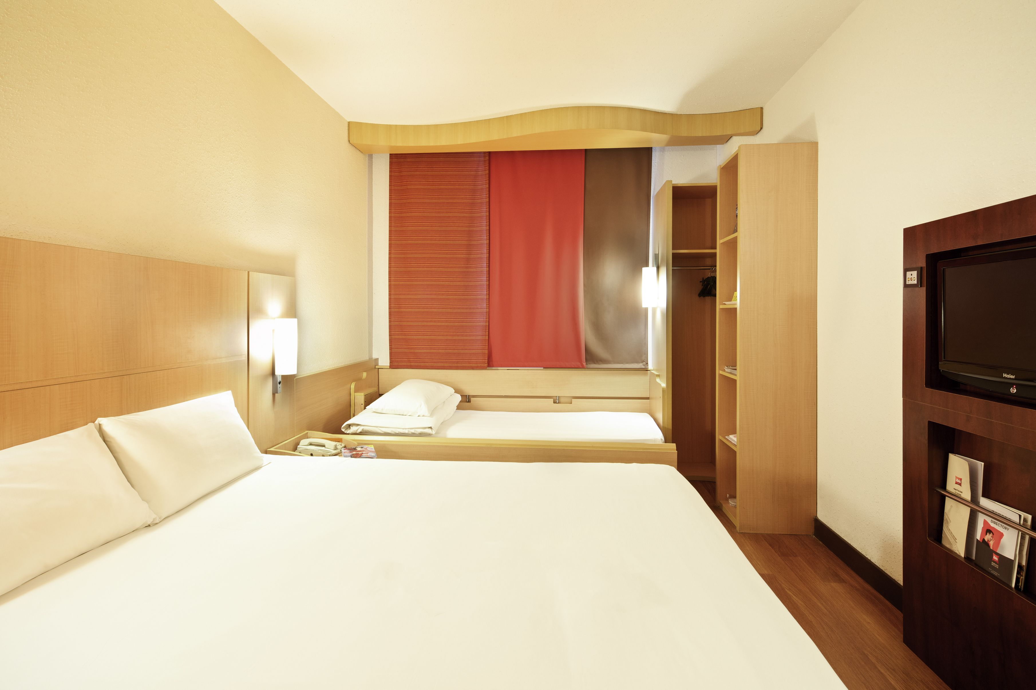 Ein Hotelzimmer mit zwei Betten, einem Fernseher, einem Kleiderschrank und einem Spiegel.