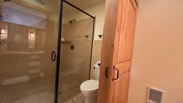 Een badkamer met een douchecabine van glas, een toilet en houten kastjes.