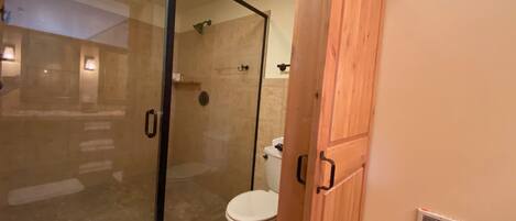Un baño con cabina de ducha de vidrio, inodoro y armarios de madera.