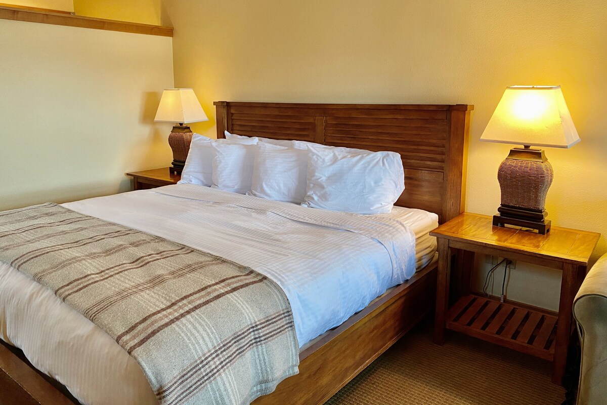 A neatly made bed with white linens and a striped blanket, flanked by two wooden nightstands with lamps.