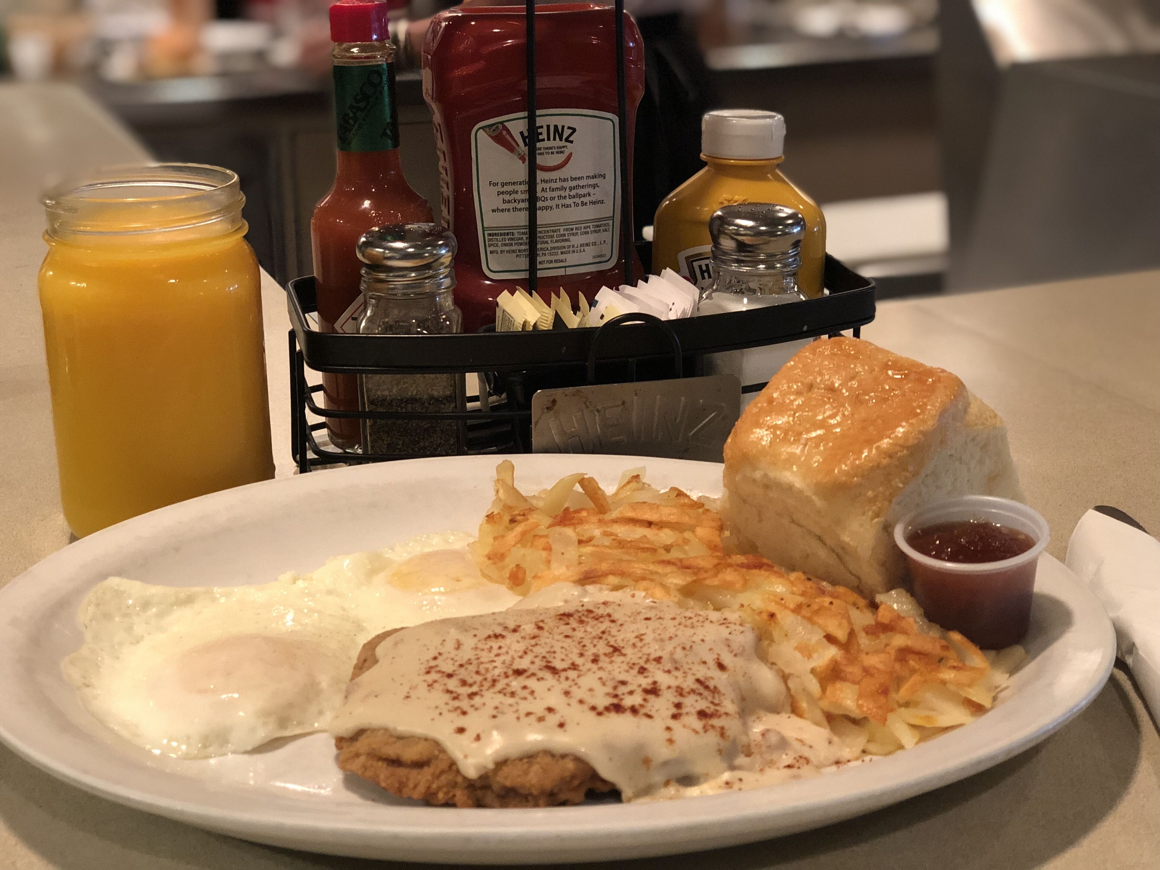 A breakfast plate with eggs, hash browns, and a biscuit, accompanied by condiments like ketchup and mustard.