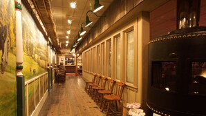 A corridor with wooden flooring, wooden chairs, a large black stove, and a mural on the wall. - Cousins Country Inn (The Dalles)