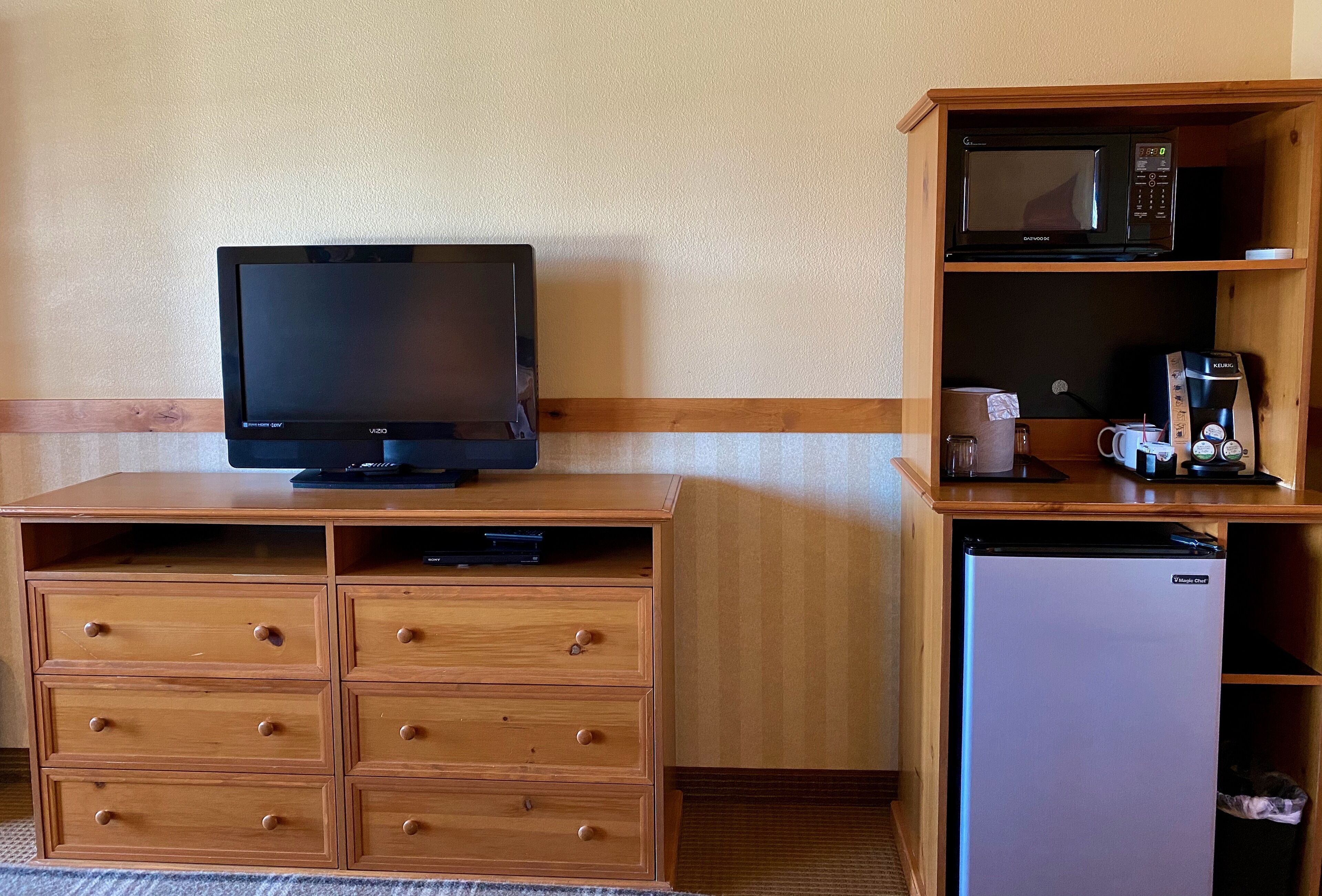 A wooden TV stand with a flat-screen TV, a microwave, and a refrigerator in a hotel room.